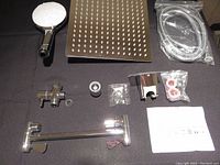 Photo showing all main components including two shower heads, extension arm, mixer valve, hose, holder and installation parts laid out on black background.