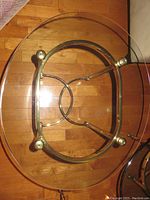 Top view of an oval brass base side table with clear glass top on a wooden floor.