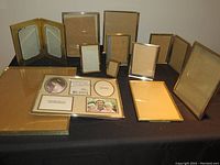 Photo showing multiple brass picture frames of various sizes arranged on a surface, some standing upright and some flat, displaying frame styles, glass fronts, and backings.