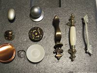 Assortment of cabinet knobs and handles displayed on foam, showing various designs and finishes including metal, porcelain, and brass.