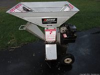 Front view of white hopper, feed chute and black engine mounted on steel frame with wheels