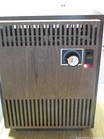 Front view of electric space heater showing woodgrain paneling, slatted vents, thermostat dial, power switch, and indicator lights.