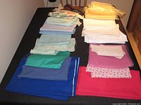 Fabric remnants in light and pastel colors including various cotton and synthetic fabrics folded and laid on a table