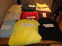 Various pieces of folded fabric including yellow embossed plush, blue, red, navy, cream, white, and purple fabrics with measurement labels.