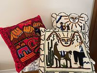 Three hand made Peruvian throw pillows with indigenous designs including sun, llama, cactus, man and vibrant red geometric pattern pillows