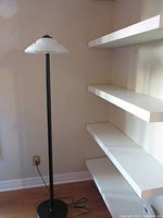 Full view of the black metal floor lamp with white glass shade, showing height and base in room corner near white shelves.