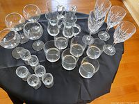 Full set of glassware displayed on a round black cloth with a wooden floor and cabinetry background