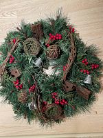Evergreen wreath with pine cones, red berries, small wooden birdhouses, and decorative woven balls placed on a wooden floor