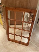 Rustic knotty pine framed mirror with 12 individual panes visible, standing upright on a floor against a door.