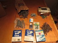 Box with assorted nails in various sizes and screws, including several blue-labeled boxes of Nails Clous by Sivaco and loose screws and nails as well.