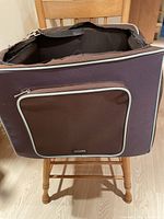 Soft fabric pet car travel seat in beige-trimmed brown fabric with zipper pocket, shown on wooden chair