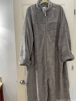 Full view of the gray plush house coat hanging on a door, showing front zipper, long sleeves with cuffs, and high collar.