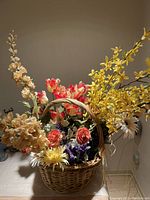 Woven basket filled with multicolored silk flowers including yellow, beige, red, and purple blooms.
