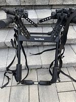Front view of SportRack bike rack showing straps and padded supports, folded and ready for mounting.