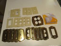 Assorted switch plates including plastic and brass types, shown all together on a flat surface with a safety switch cover still in package.