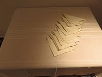 Photo showing oval cream colored tablecloth covering a table with 8 neatly folded matching napkins on one side.