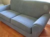 Blue upholstered Thomasville sofa with two detachable seat cushions and fixed back on wooden floor.