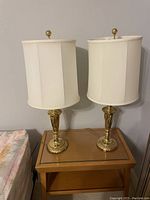 Front view of two brass lamps with white silk drum shades set on a small wooden table.