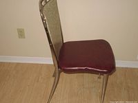 Side view of one vintage kitchen chair showing stainless steel legs, patterned backrest upholstery in beige plastic, and dark red re-upholstered seat.