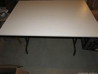 Top view of one utility table showing white MDF top surface and brown steel folding legs.