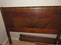 Close-up view of the vintage solid mahogany headboard with visible book match veneer pattern and some wear and damage on the veneer surface.