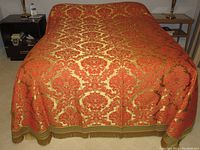 Full view of the vintage red and gold brocade bed cover draped over a full bed, showing the intricate pattern and gold fringe.