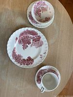 Set of a cup, saucer, bowl, dinner plate, and bread plate showing pink floral pattern and scalloped edges on wooden table