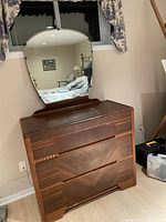 Front and side angle view of vintage waterfall dresser with attached mirror. Shows the wood grain, drawer fronts, and condition of finish.