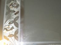 Close-up of floral embossed design along left edge of the mirror showing flowers and leaves embossed in glass with beveled edging.