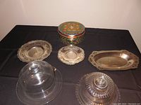 Overview of 3 small serving platters, 2 glass covered servers, large roaster, and vintage cake tin.