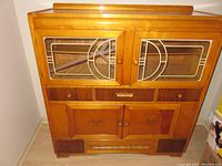 Full view of upper part of light wood vintage kitchen armoire showing glass window panes with geometric design in upper doors and wooden lower doors.