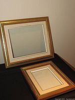 Two large picture frames with gold and cream inner borders, one leaning against wall and the other lying flat.