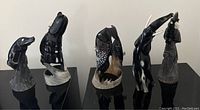 Group photo of five hand-carved black and white animal sculptures on black pedestal