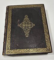 Top view of closed Bible showing dark brown leather cover with ornate gold gilt embossing along border and central cross pattern.