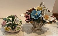 Wide shot showing both vintage porcelain flower bouquets, one handled basket style and one smaller cluster bouquet.
