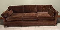 Front-facing view of chocolate brown 3-seater mid-century couch with removable cushions.