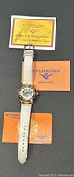 Full watch with strap laid flat on gray surface with Stuhrling Original cards nearby.