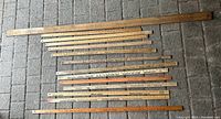 Top view of 14 wooden yardsticks laid out on grey paving stones showing varying lengths and conditions