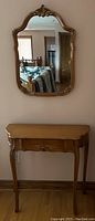 Front view of vintage side table with single drawer and vintage scalloped mirror hung above it.