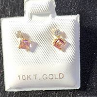 Photo showing pair of 10K yellow gold earrings with pink tourmaline and diamond on a white display card marked '10K T. GOLD'