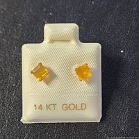 Pair of 14K white gold stud earrings with square-cut citrine stones displayed on a white holder marked '14 KT. GOLD'.