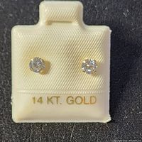 Close up front view of the pair of stud earrings on cream-colored display with 14 KT GOLD stamp.