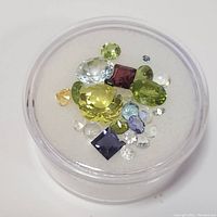 Overhead photo showing all assorted faceted gemstones inside round plastic container, including peridot, amethyst, blue topaz, moonstone, and yellow gem.