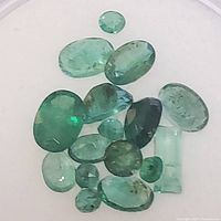 Close-up photo of multiple oval and one rectangular cut green emerald gemstones displaying varying shades of green and natural inclusions.