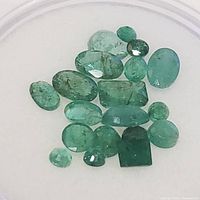 Photo of 19 loose emerald gemstones of varying shapes and sizes, showing color, cut, and clarity.