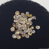 Close-up photo showing the various round-cut diamonds with different colors on a black foam background.