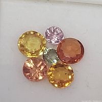 Close-up of six faceted colorful sapphire gemstones in various hues including yellow, orange, pink, and green.