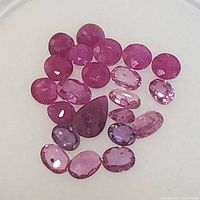 Top view showing 24 loose rubies in assorted cuts including round, oval, pear, and rectangular shapes with various pink and red shades.
