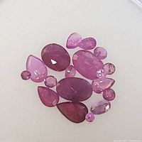 Close-up of red to pink faceted ruby gemstones in different shapes such as oval, pear, and round.