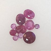 Nine faceted ruby gemstones of varying shapes and sizes on a white background.